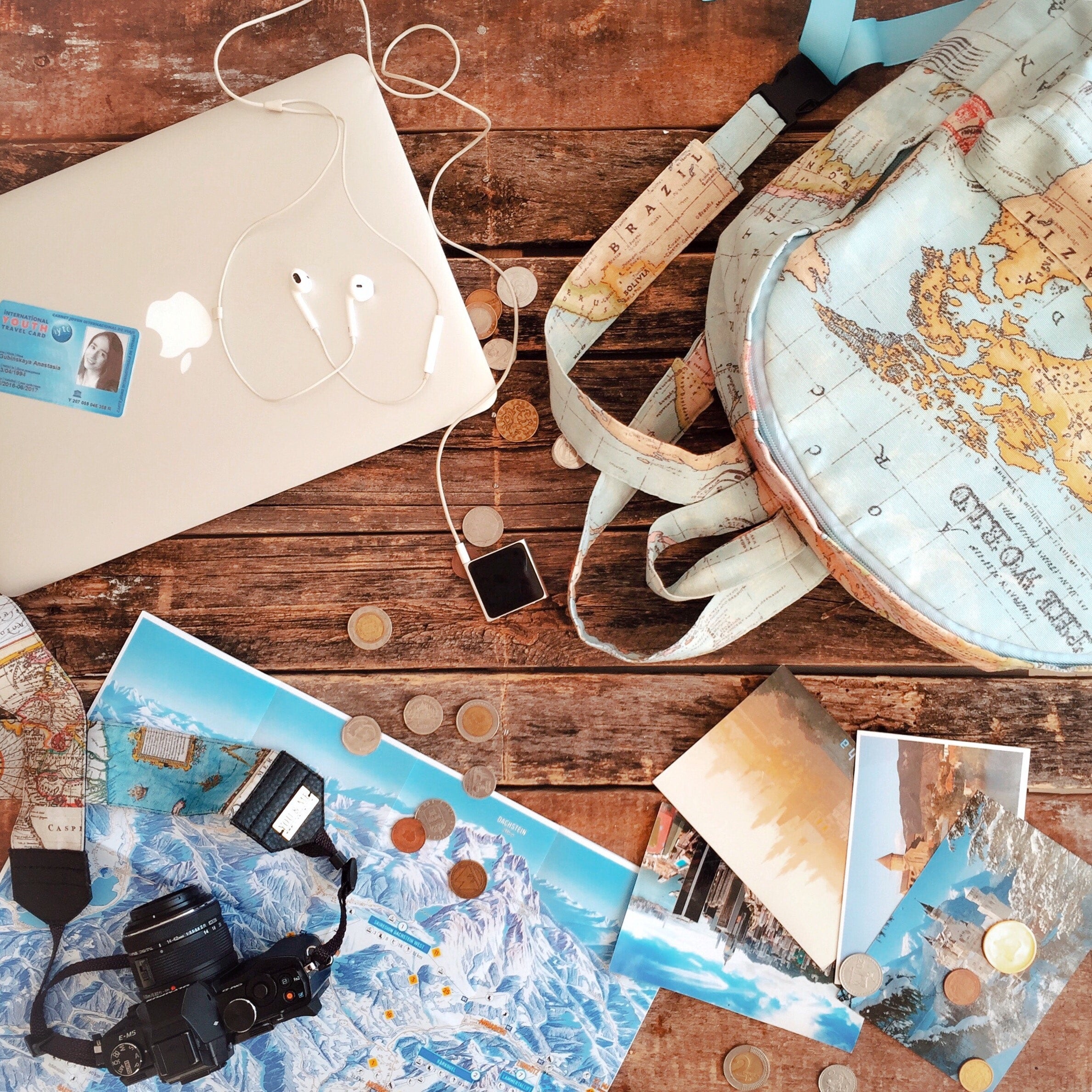 An image of a desk with a laptop, student ID, backpack, and some money from  various countries. 