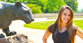 Student posing in front of Mountain Cat statue