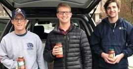 three students holding pasta sauce