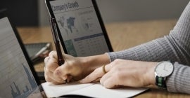 woman writing something down and looking at graphs on two computers