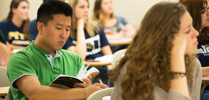 student in a classroom reading a book
