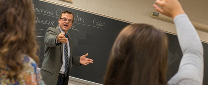 student raising her hand to ask the professor a question